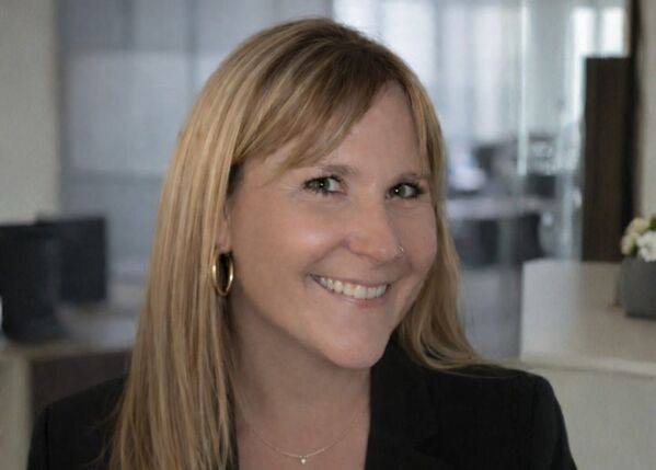 Frau mit langen blonden Haaren lächelt in einer Büroumgebung.